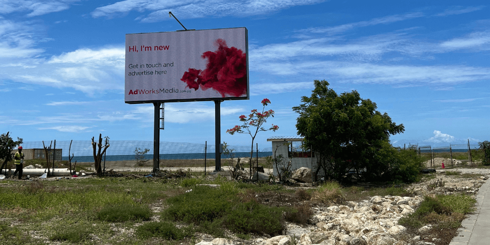 Large AdWorks Media digital billboard beside a coastal road under a bright blue sky.