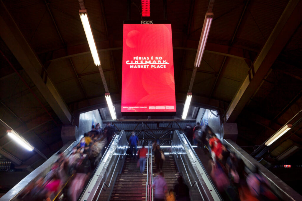 Digital out-of-home ad for Cinemark Market Place displayed above escalators in a busy transit station.