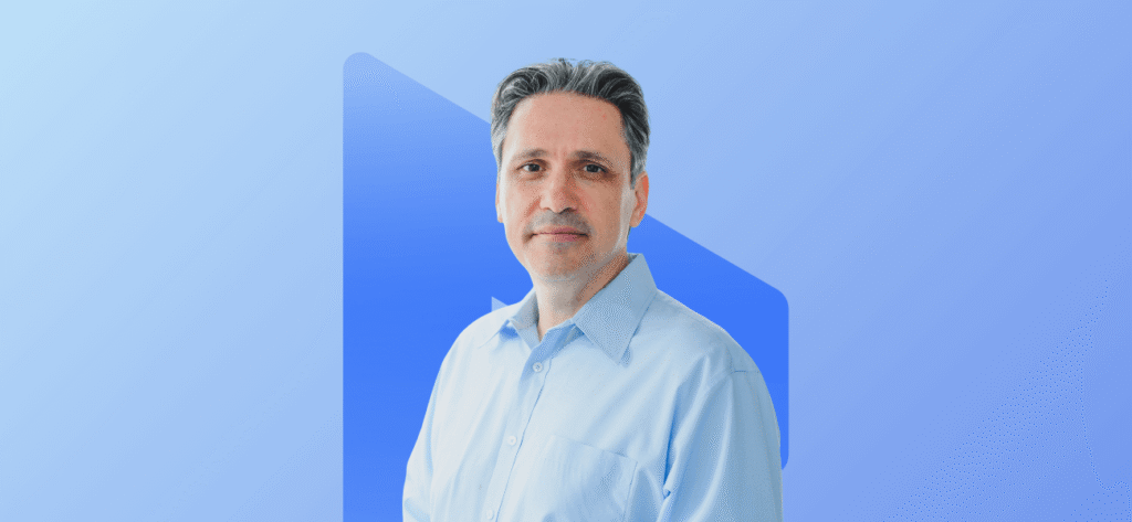 Portrait of a man in a light blue shirt against a blue branded background.