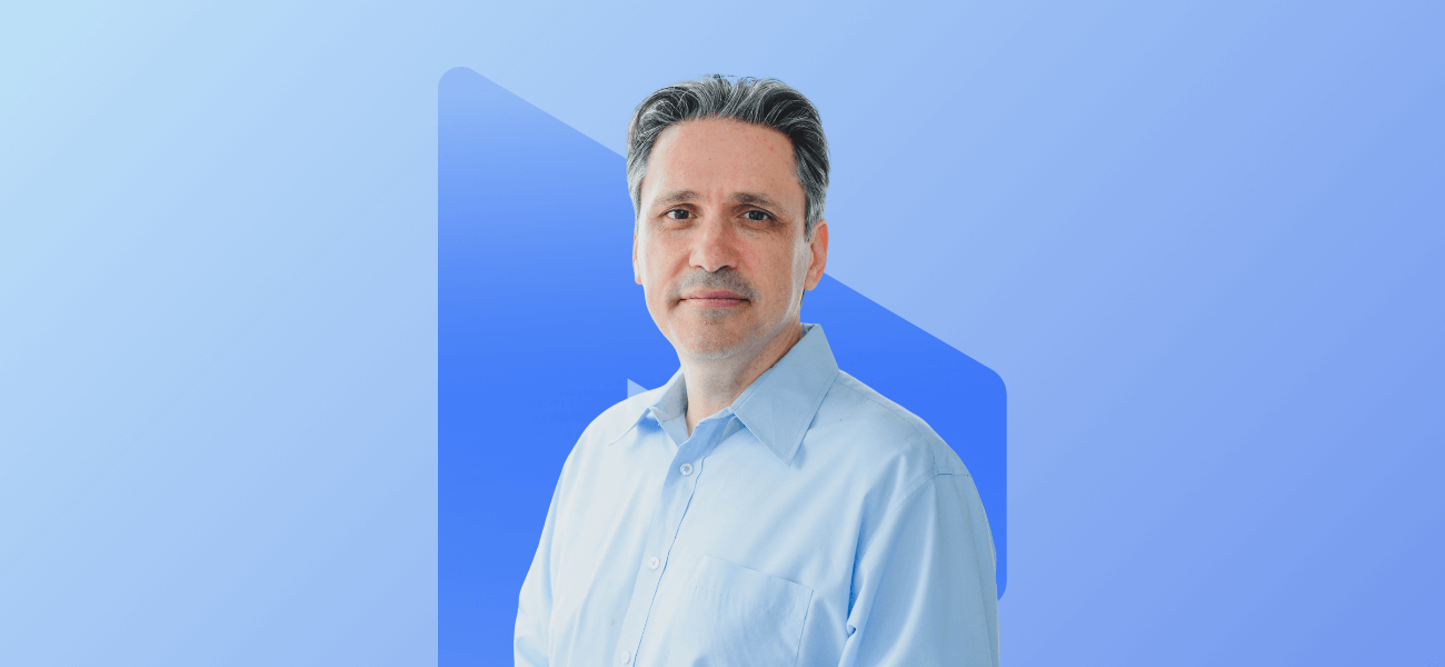 Portrait of a man in a light blue shirt against a blue branded background.