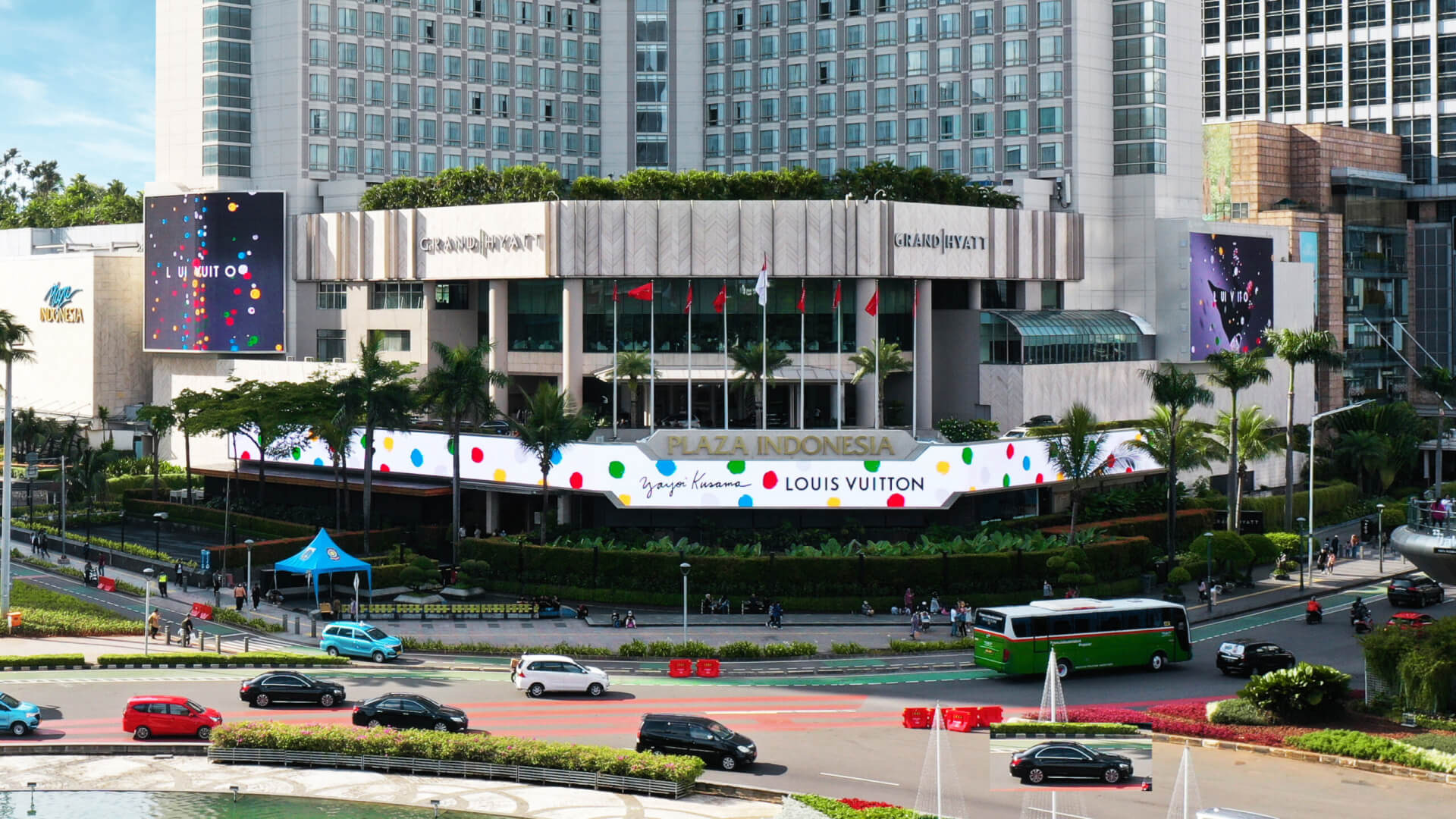 Large digital advertising displays on the exterior of Plaza Indonesia shopping center overlooking a busy city street.