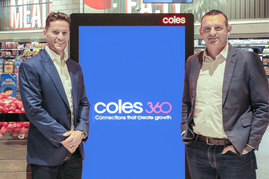 Two men standing beside a digital display featuring the Coles 360 logo inside a Coles supermarket.