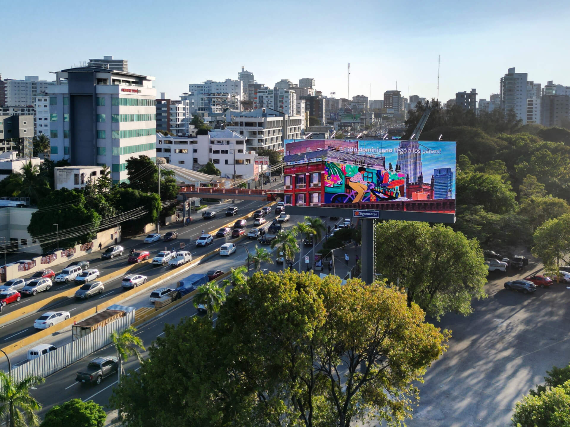 Large digital out-of-home billboard overlooking a busy city highway surrounded by high-rise buildings and greenery.