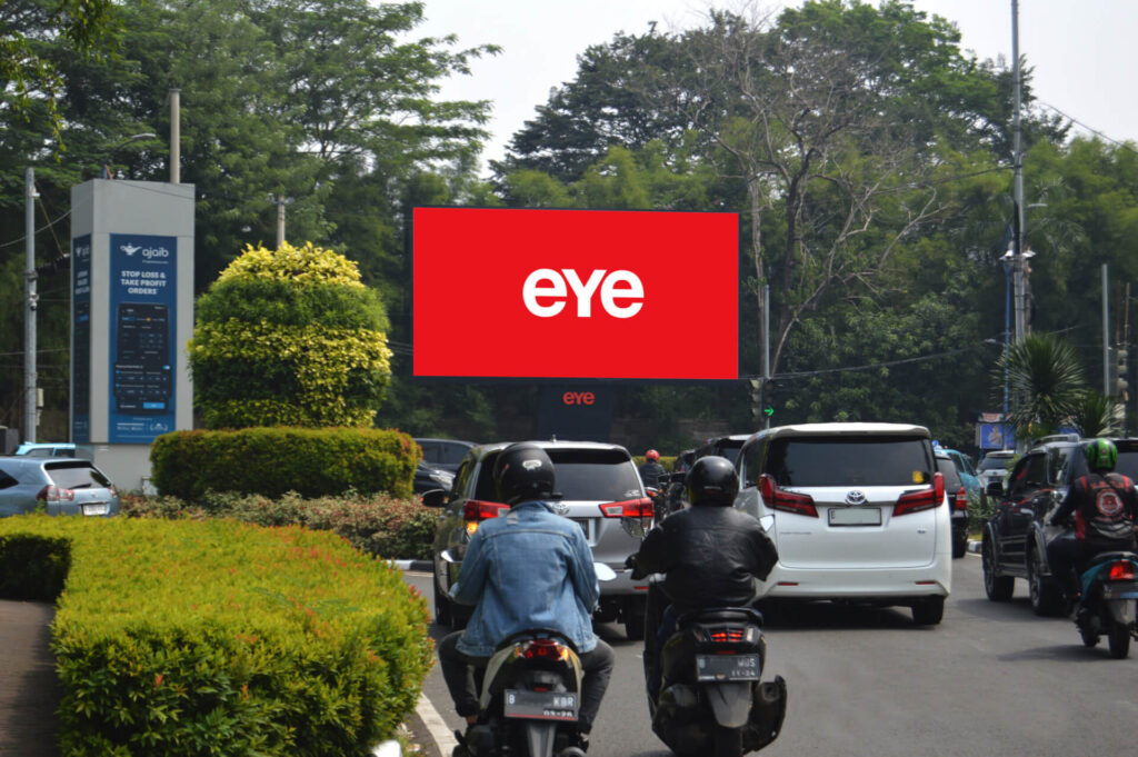 Large Eye digital billboard overlooking cars and motorcyclists on a busy tree-lined road.