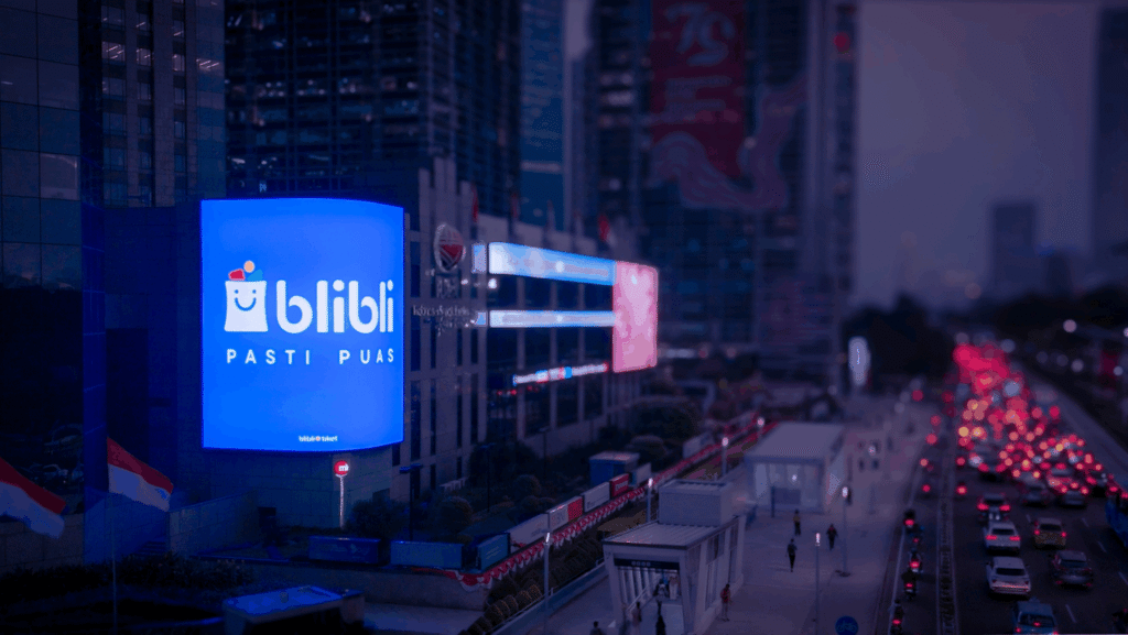 Digital out-of-home billboard illuminating a busy urban street at night with heavy traffic in Indonesia.