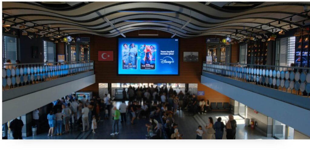 Large Disney+ digital advertisement displayed above a crowd inside a busy indoor venue.