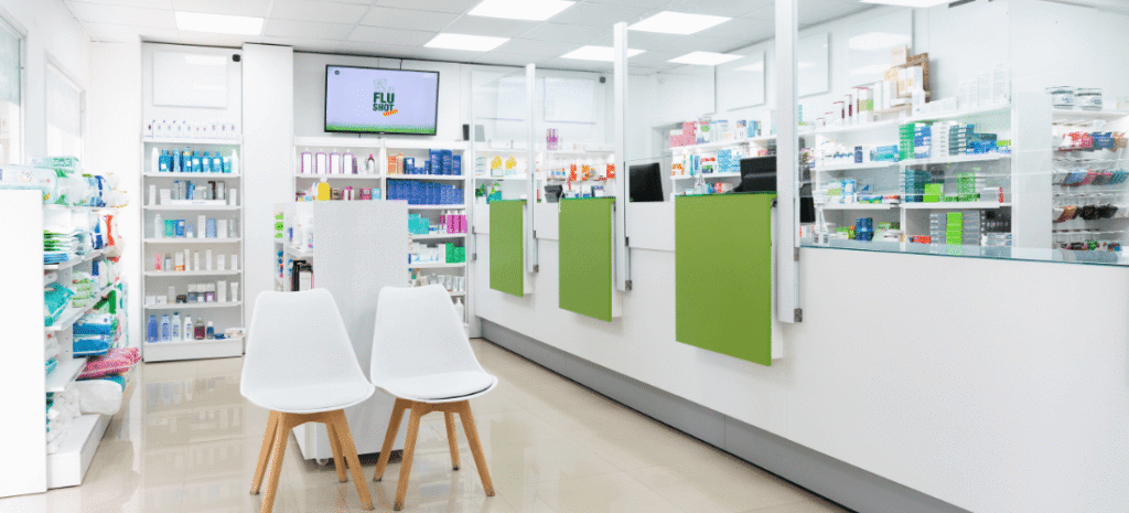 Modern pharmacy interior featuring prescription counters, waiting chairs, product shelves, and a digital display.