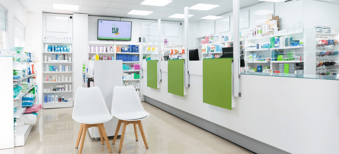 Modern pharmacy interior featuring prescription counters, waiting chairs, product shelves, and a digital display.