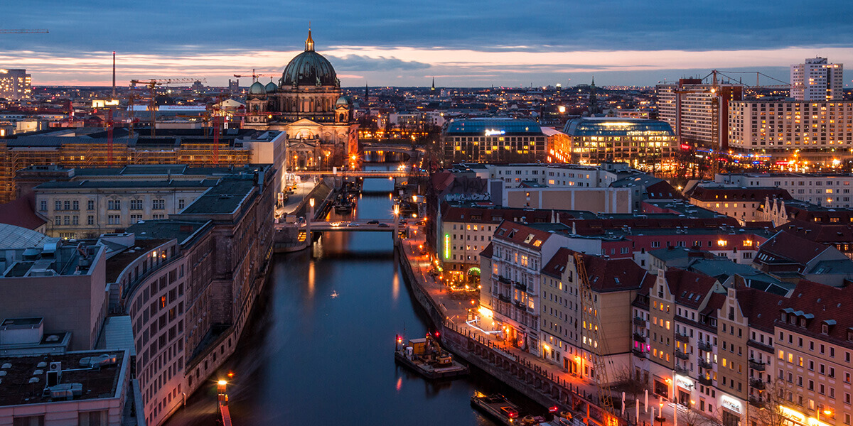 Aerial view of Berlin at dusk, with the Berlin Cathedral overlooking the Spree River and illuminated city buildings.