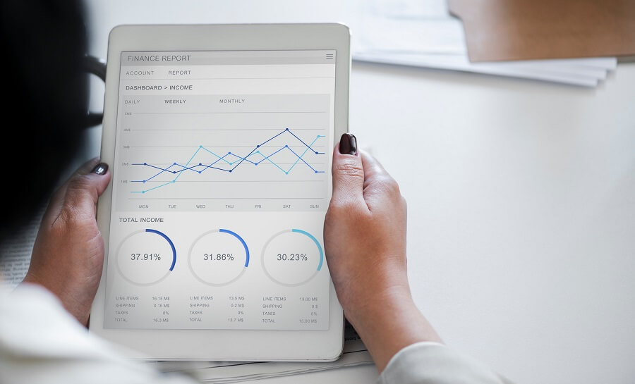 A woman holding a tablet. On the tablet's screen are charts and figures relating to finances. Reviewing data in this way is an important method of determining DOOH campaign effectiveness.