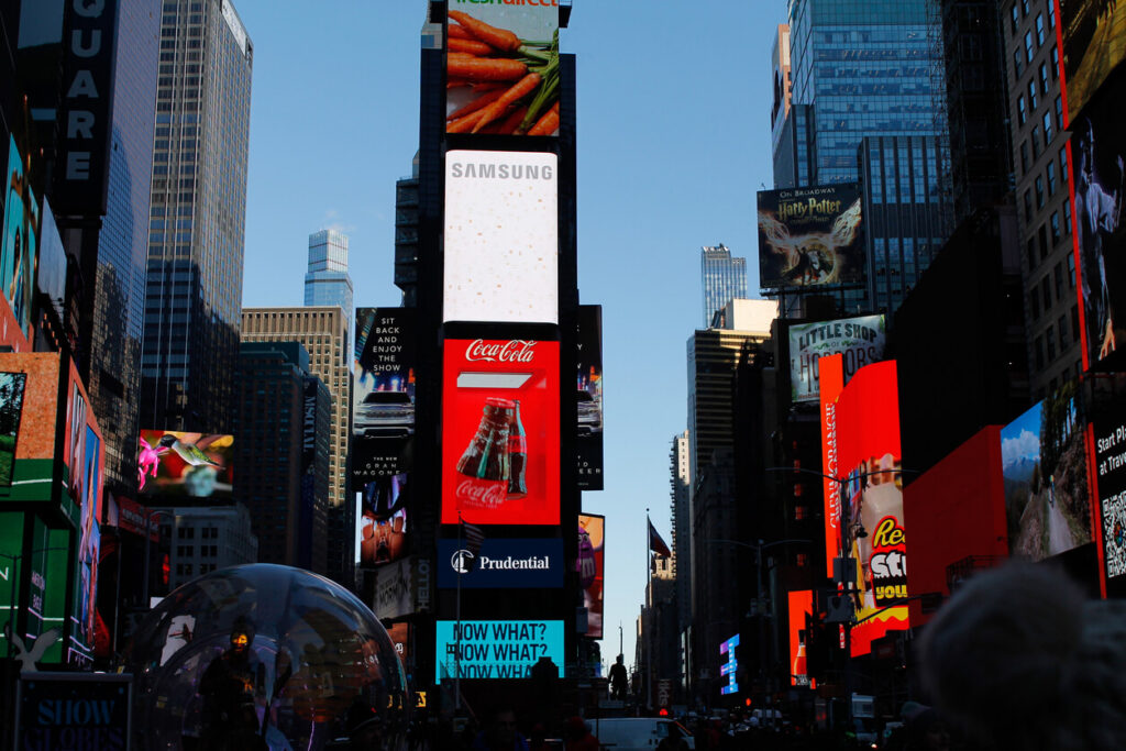 Times Square during the day featuring large digital billboards and out-of-home ads from major brands.