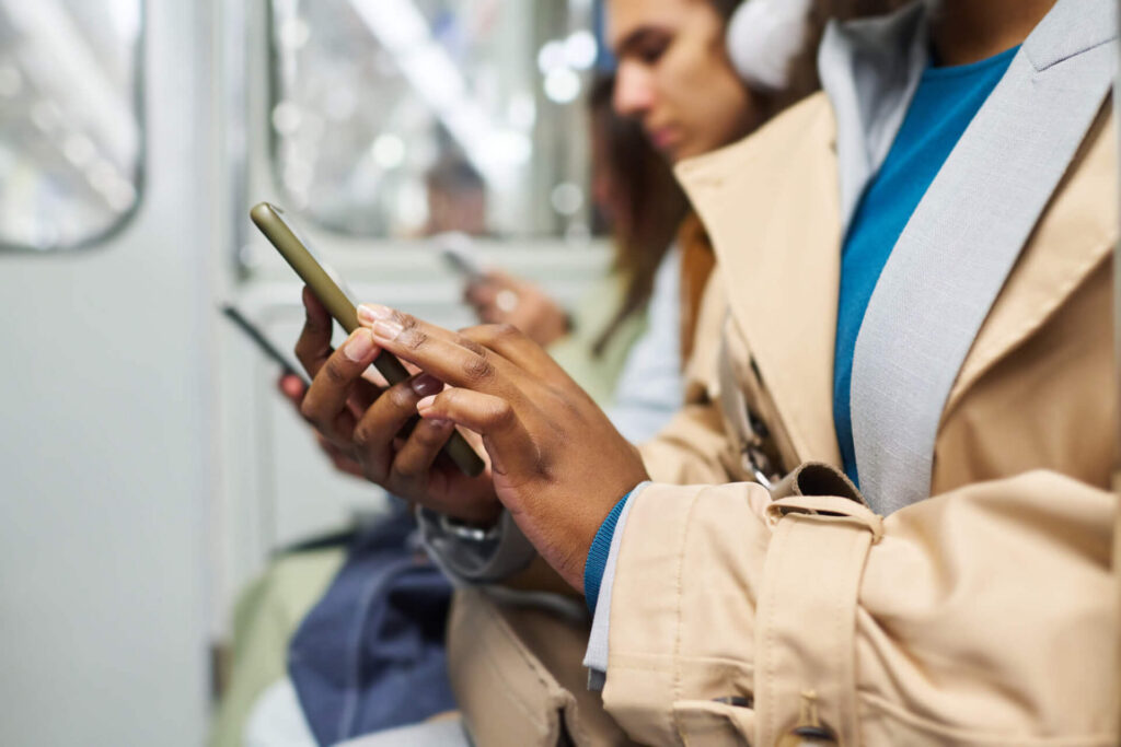 Close-up of commuters using smartphones while seated together in a public transit setting.