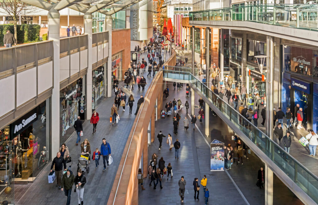Busy multi-level shopping centre filled with shoppers walking past retail stores and storefronts.