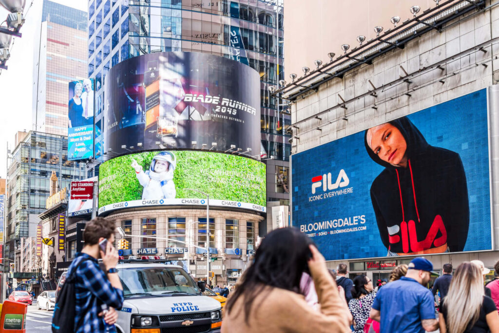 Large digital billboards featuring FILA, Chase, and Blade Runner 2049 advertisements in a busy New York City shopping district.