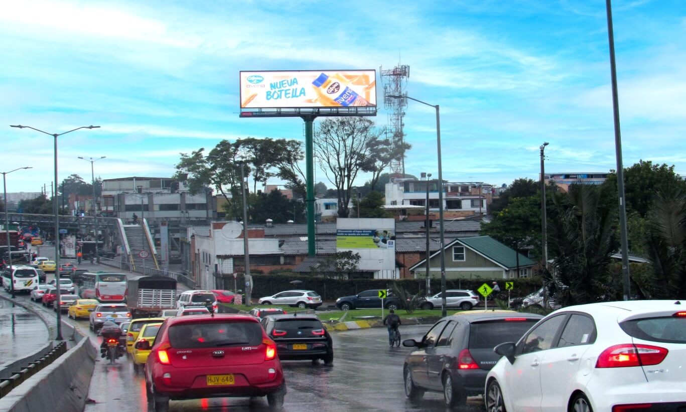 Busy city roadway with traffic passing beneath a large digital billboard advertising Avena.