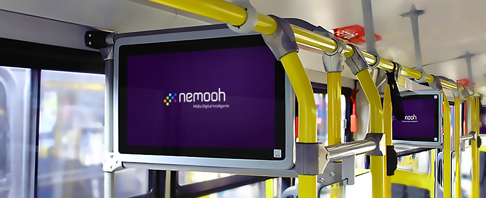 Digital advertising screens mounted inside a city bus above yellow handrails.