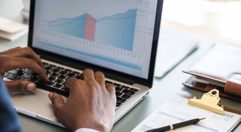 A man sitting at a computer looking at a chart of climbing sales. In terms of CPMs, programmatic direct would likely result in greater revenue.