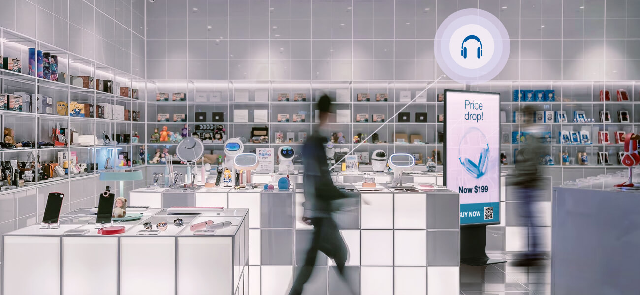 Digital advertising display promoting headphones inside a modern electronics store as shoppers walk by.